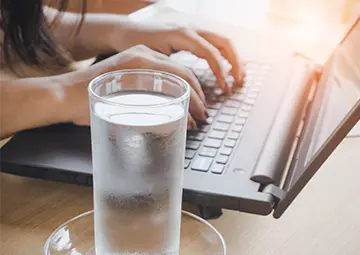 Woman on laptop next to a glass of water